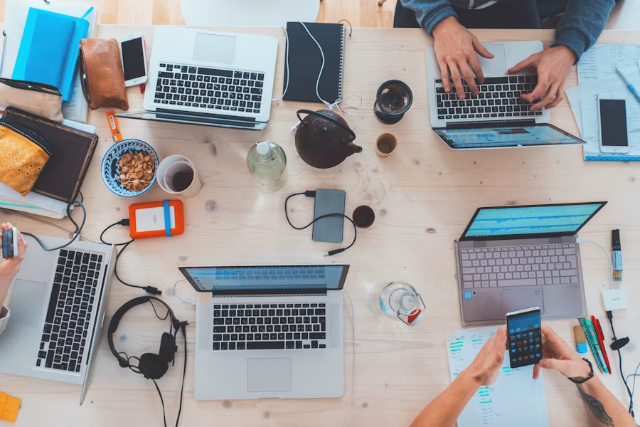 Vista dall'alto di una scrivania condivisa con laptop e persone al lavoro